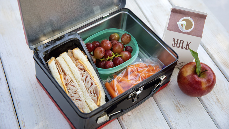 generic metal lunchbox with a sandwich, grapes, carrots, apple and carton of milk