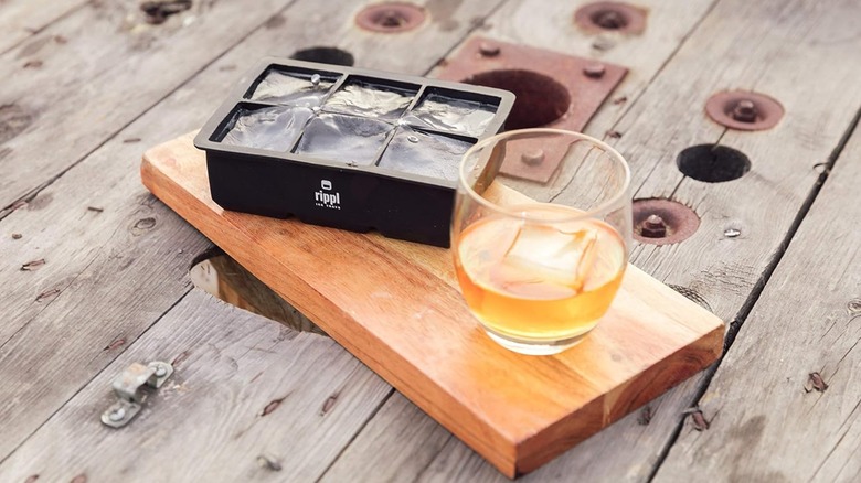 Ripple large ice cube tray on a wooden block with a glass of spirit on a wood background