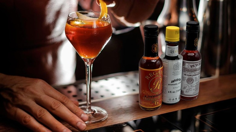 The set of three Bitters Triple Play bitters on a bar top next to a cocktail