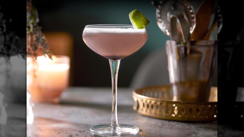A cocktail in a Libbey coupe glass with a blurred candle and cocktail tools in the background