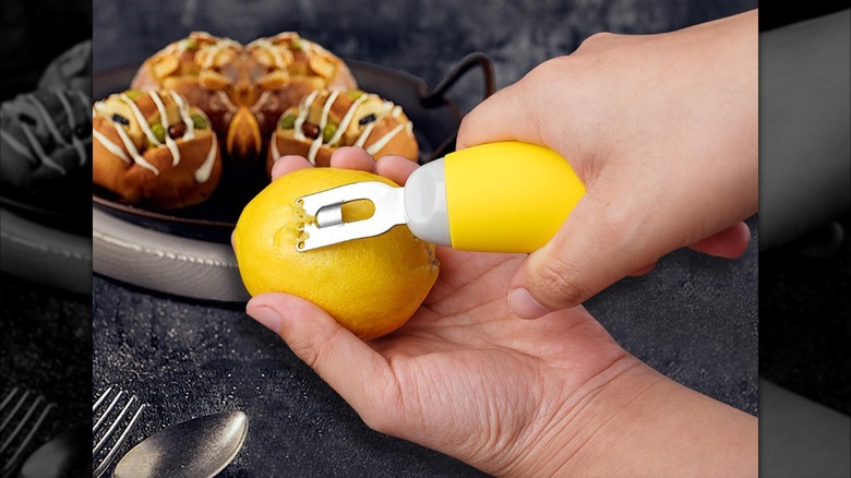 Close-up of someone using the Kithendao peeler and zester combo on a lemon with blurred food on a tray in the background