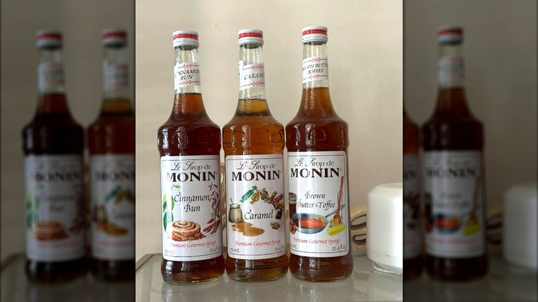 Three bottles of flavored Monin flavored syrups lined up on a tabled