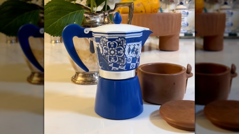 Blue and white espresso coffee maker on a table next to a wooden cup
