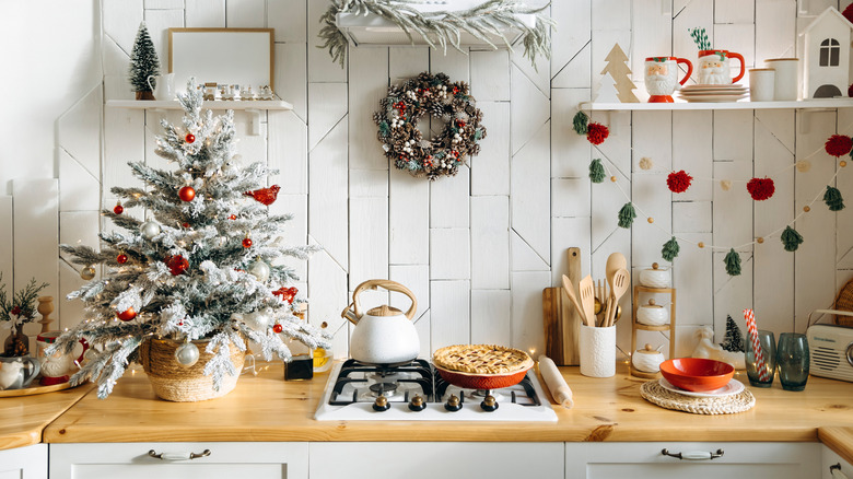 A simple white kitchen decorated for Christmas with ornaments, Santa mugs, and a small tree