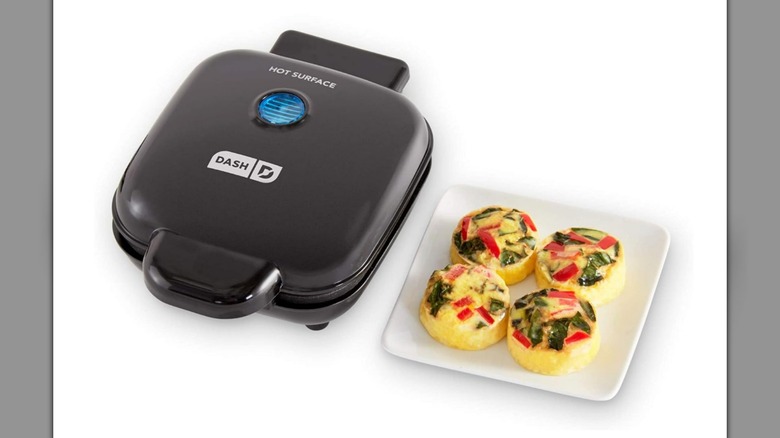 A Dash Deluxe Egg Bite Maker and four egg bites on a plate on a white background