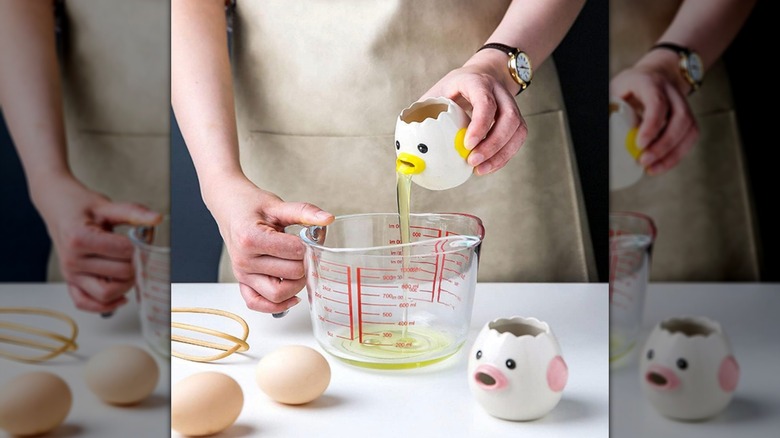 A hand using a LuoCoCo Egg Separator to pour egg whites into a measuring cup