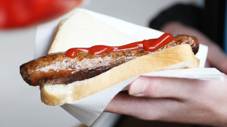 A person holding a sausage sanga, a sandwich made with grilled sausage and bread