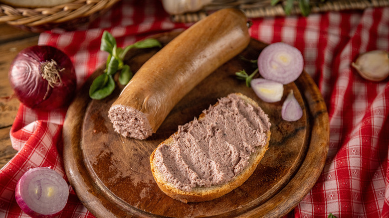 Liverwurst on a wooden board with some of it spread on bread on the side