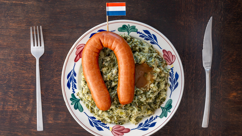 Rookworst served over stamppot on a wooden table with a fork and a knife on each side