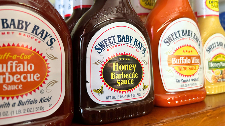 Close up of several Sweet Baby Ray's bottles lined up on a wooden shelf