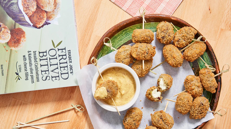 Fried olive bites on plate with dipping sauce and the light green box nearby