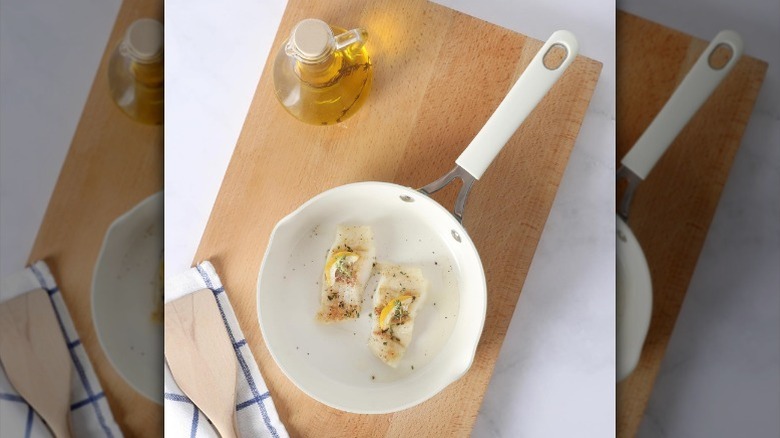 Frying pan on wood cutting board with fish