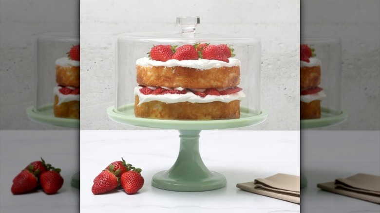 Cake on cake stand with glass lid on counter with strawberries