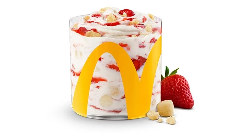A McFlurry in a clear cup next to a strawberry and cheesecake pieces
