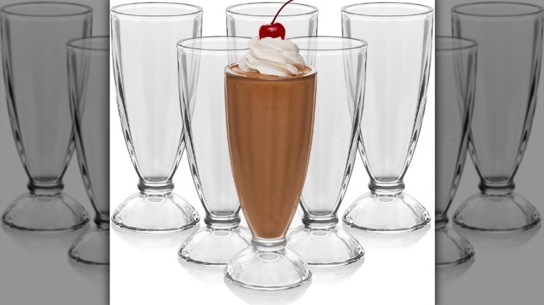 Chocolate milkshake and empty fountain shoppe glasses against white background.