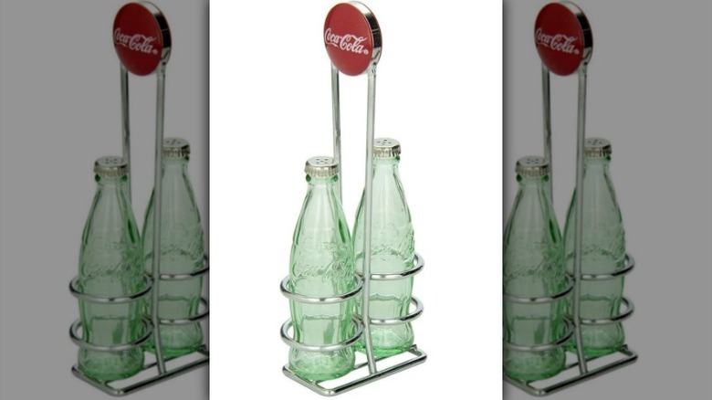 Coca-Cola salt and pepper shakers in metal holder against white background.