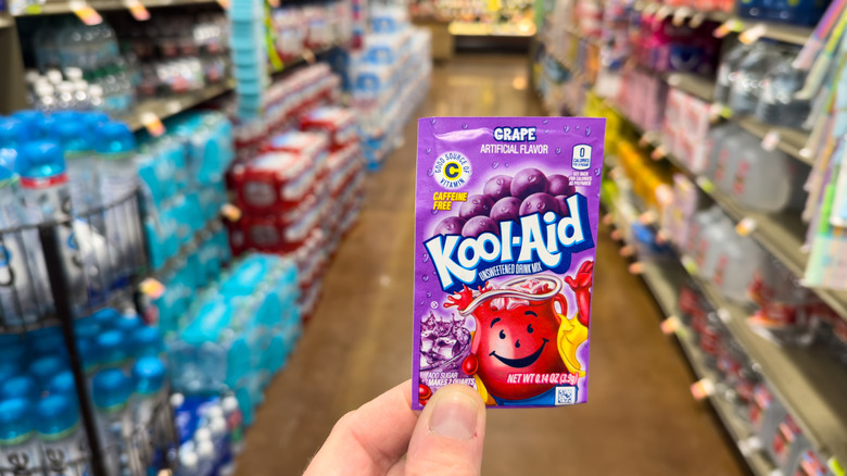 A hand holds a sachet of Grape Kool-Aid