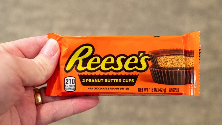 A hand holds a package of Reese's Peanut Butter Cups