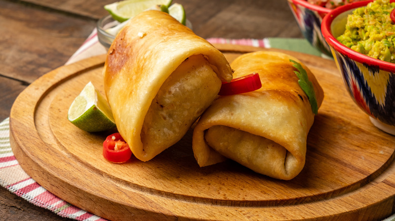 Two chimichangas on a wooden board