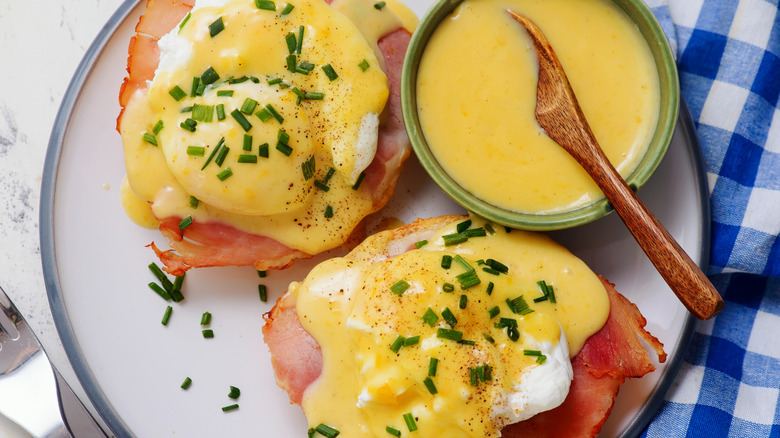 Close up of classic eggs Benedict on a white plate with a side ramekin of hollandaise sauce