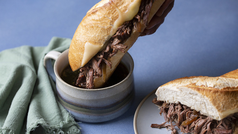 Classic French dip sandwich being dunked into a bowl of au jus