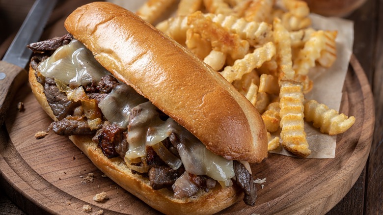 A Philly cheesesteak with fries on a wooden board