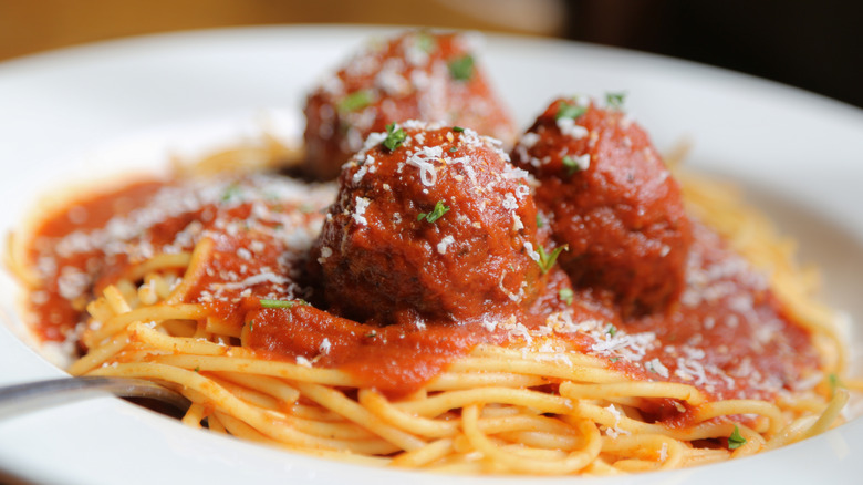 Close-up of three meatballs on a plate of spaghetti, topped with chopped herbs and grated Parmesan cheese