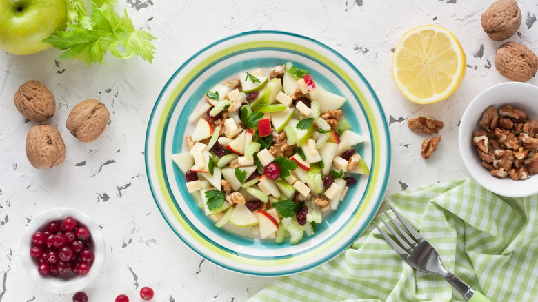 Waldorf salad in decorative bowl surrounded by grapes and walnuts