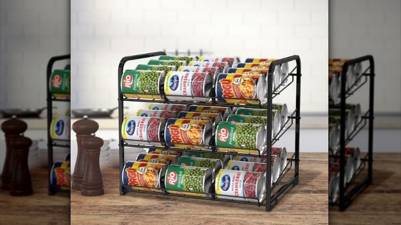 Cans in three-tiered metal can dispenser on kitchen counter.