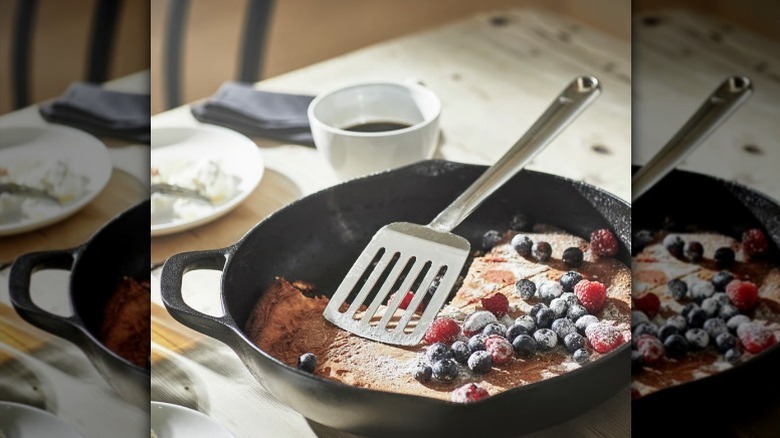 Metal spatula with clafoutis and berries in a cast iron pan on a tabletop.