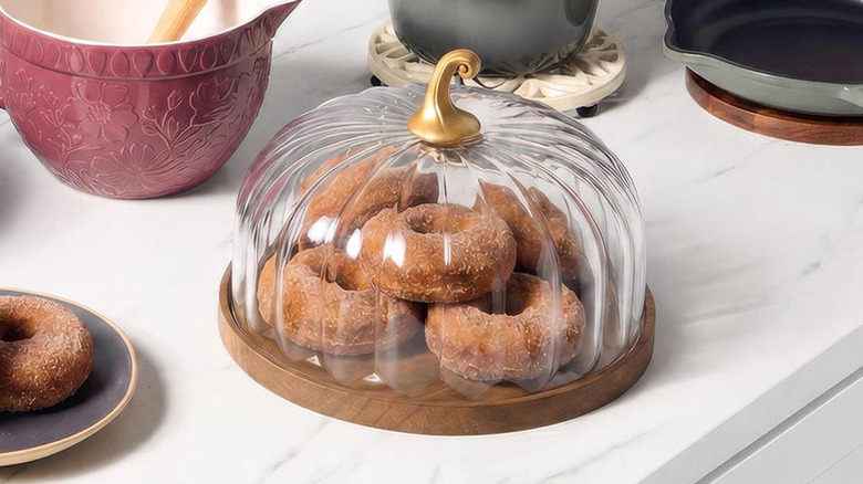 The Crofton Glass Stem Pumpkin Dome on a countertop, storing several donuts