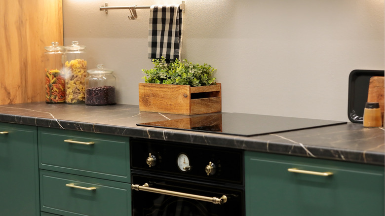 Contemporary kitchen with dark, gold-veined laminate countertops on green cabinets with brass hardware
