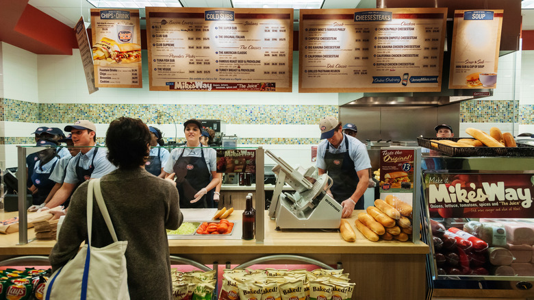 Jersey Mike's employees making sandwiches behind counter.