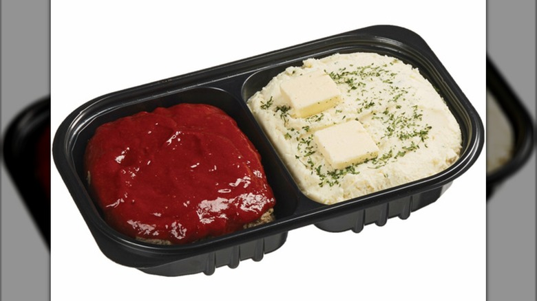 A black plastic divided tray of meatloaf and mashed potatoes with butter