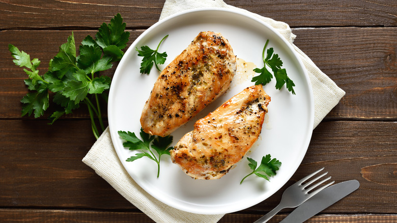Roasted boneless, skinless chicken breasts with seasonings and parsley on a white plate