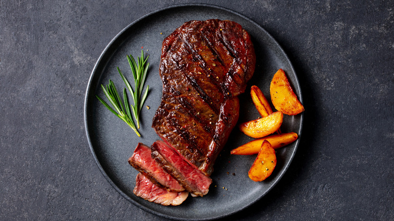 A seared medium rare steak on a plate, with glazed carrots and rosemary