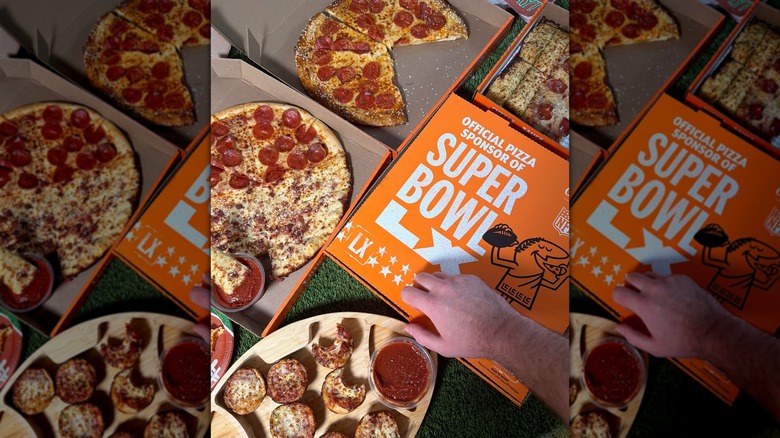 A hand opening a Little Caesars box, next to three already open pizza boxes