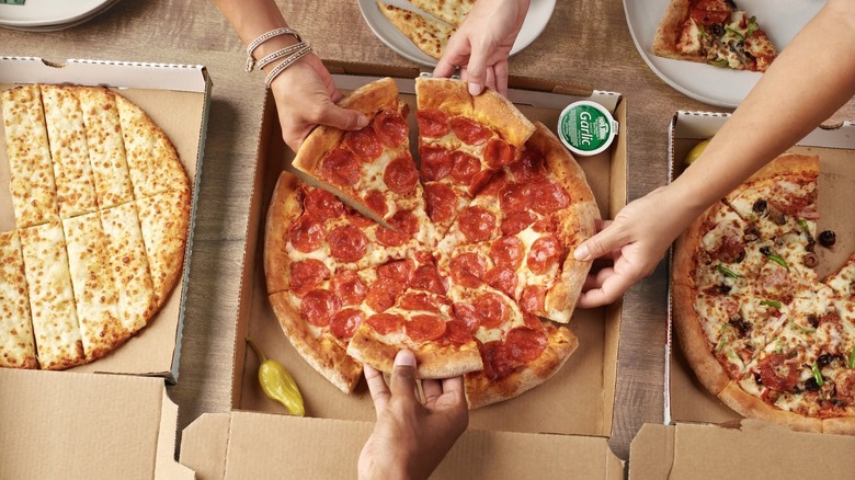 Four hands taking slices from a Papa Johns pepperoni pizza