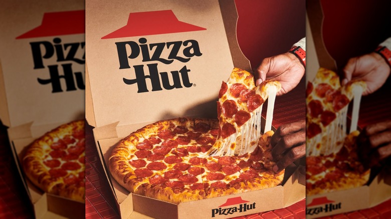 A hand taking out a slice of cheesy pepperoni pizza from a Pizza hut box