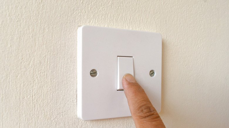 finger pressing on light switch on wall