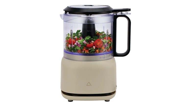 A beige colored mini food chopper with tomatoes, red onion, and cilantro inside