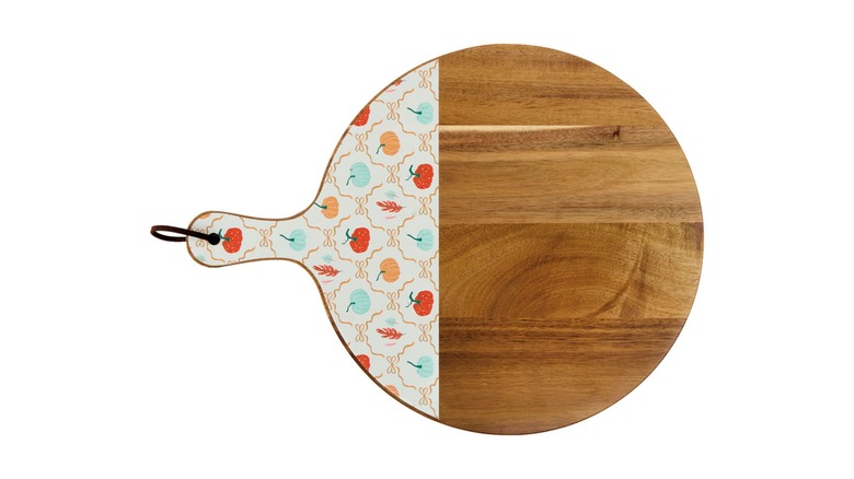 A round serving board with a wooden finish and white enamel with red, orange, and blue gourds on a print design