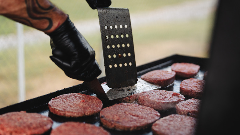 A chef pressing raw burger patties on a flat top griddle