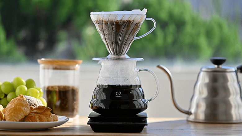 Hario v60 on coffee pot with kettle, coffee grounds, croissants, and grapes