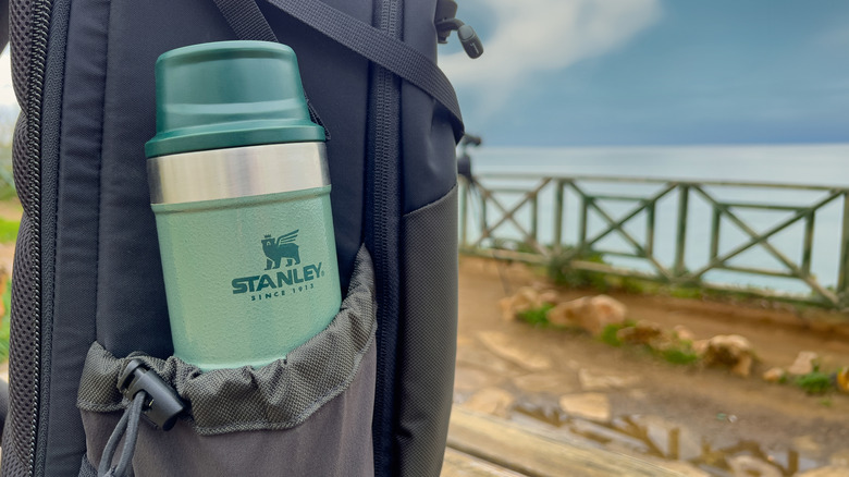 A green Stanley water bottle in a backpack with a sky background