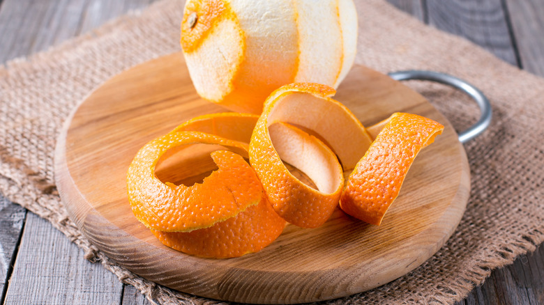 Orange rinds sitting on a round, wooden board in front of the peeled fruit