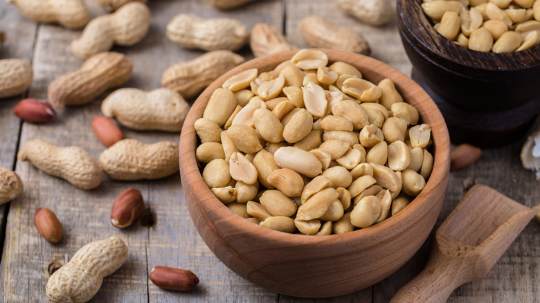 Salted peanuts in a small wood bowl surrounded by shelled peanuts