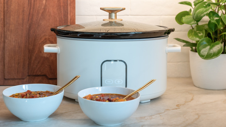 White slow cooker with two white bowls of stew