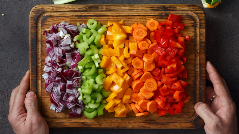 Hands holding cutting board of colorful chopped veggies