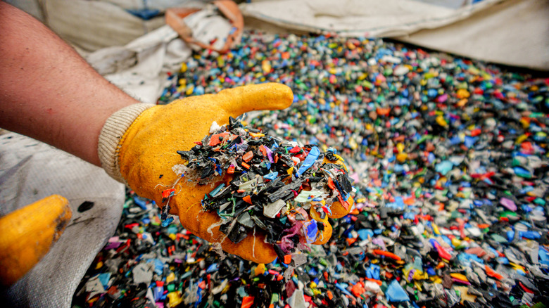 A gloved hand reaching into a huge container of plastic refuse